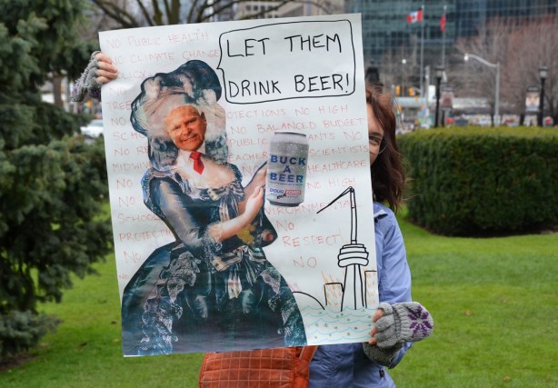 a woman holds up a sign at a protest that says let them drink beer. with a picture of Doug Ford as Marie Antoinette