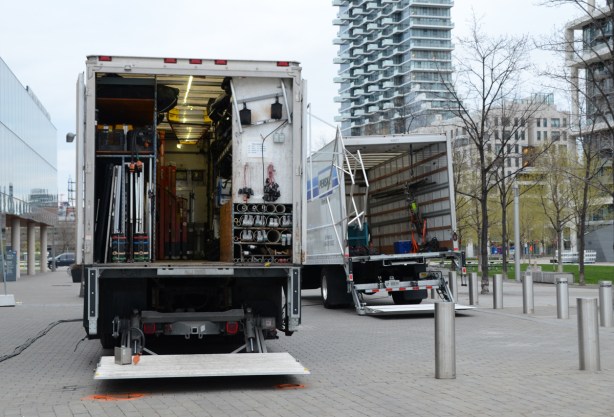 the back of two large trucks with their doors open as cables, tools and other equipment for filming is being load back into the trucks 