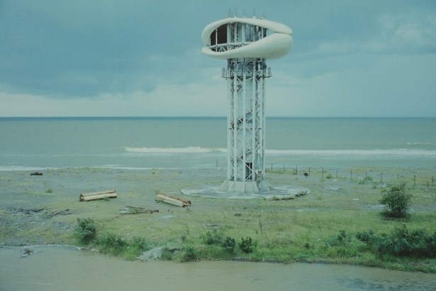 large photo of a oval shaped structure on the top of a tower, on the coast, surrounded by barren land, abandoned building, in Anaklia Georgia (former USSR republic) 