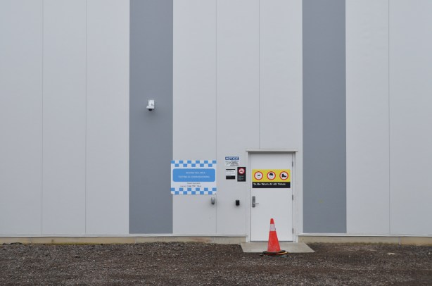 exterior of new crosstown maintenance facility with double grey stripes, a doorway with many warning signs.