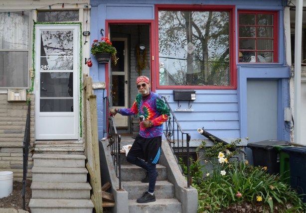 Johnny in a tie dyed shirt standing on the front steps of a blue house with red trim