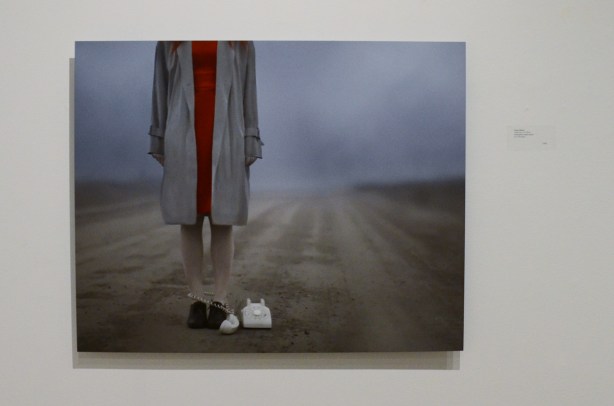 A Patty Maher photo of a woman standing on a deserted country road with an old rotary phone at her feet, her head has been cropped out of the photo, foggy in the background