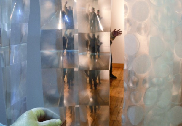 art installation that uses strips of plastic shower curtain. The squares in the plastic make the person on the other side appear many times - one each in every square