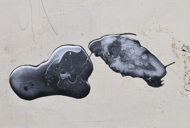 two black and white photo paste ups that look like ameobas or primitive life forms on a concrete wall, outdoors, 