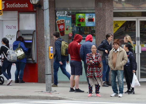 people at an intersection, a woman in a red and black plaid jacket and pink shoes 