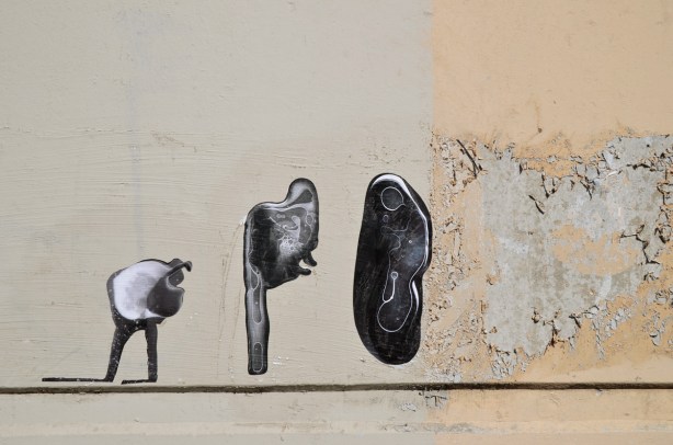 three black and white photo paste ups that look like ameobas or primitive life forms on a concrete wall, outdoors, 