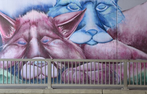 part of a mural by Christopher Ross on an underpass wall in pinks and blues, a blue animal and a pink animal