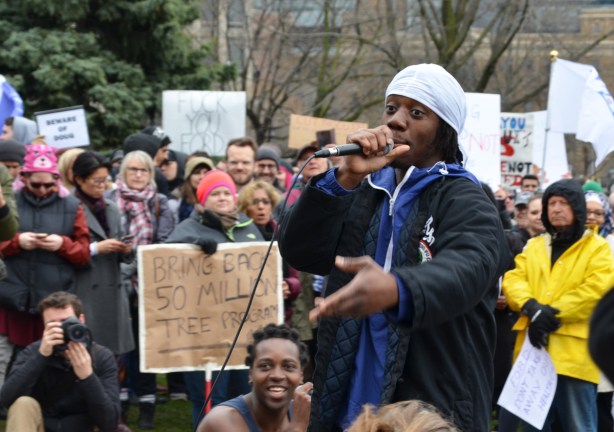 a young black man is performing a rap song in front of a crowd at a protest 