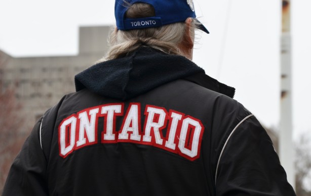 the back of a man whose baseball cap says Toronto on the back and his black jacket says Ontario on the back 