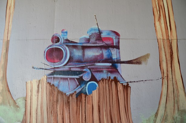 part of a mural by gawd, a little railway engine sits on a tree stump