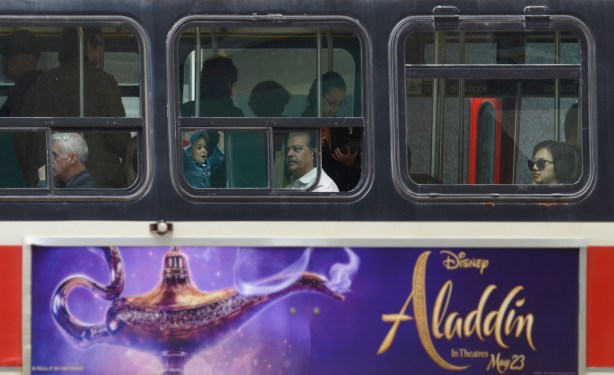 a man and a young girl look out the window of a TTC streetcar with a poster on the side advertising Aladdin movie 