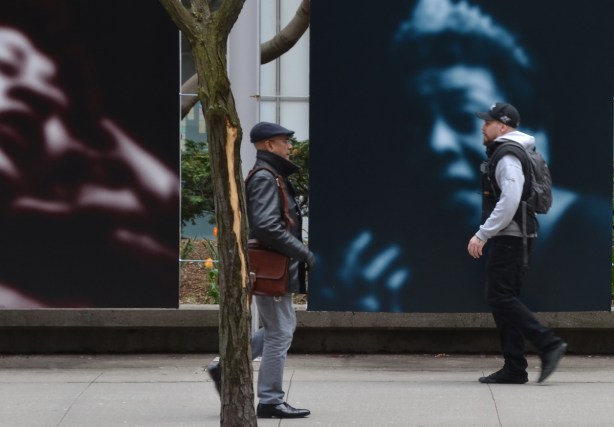 two men walk past two large photos on King Street, Slow Fade to Black photo by Carrie Mae Weems, one is blue and black and the other is burgundy and black 