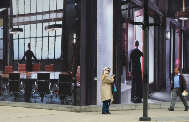 two large photos mounted on two walls that meet at the corner of King West and Widmer, two people walking them including a woman in a head scarf 
