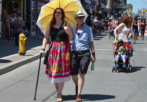 a couple strolls down Yonge St in dyke march, one with cane and large yellow umbrella