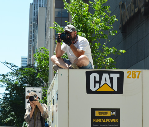 two photographers at a parade, onei s sitting on top of a large generator (trailer)
