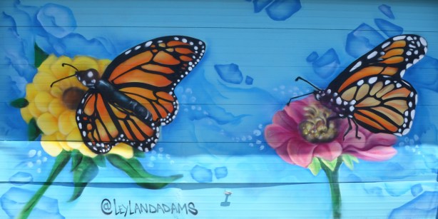 a mural with two monarch butterflys by a flower, bright blue background, garage door 
