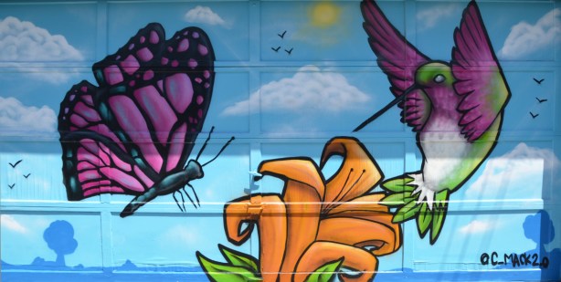 mural on a garage door in an alley, large purple and black butterfly, an orange tiger lily flower and a hummingbird 