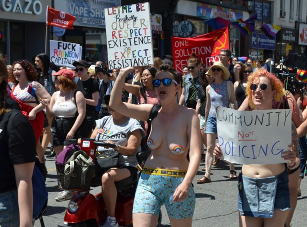 topless woman walking with other women in a dyke march, holding signs and chanting or protesting