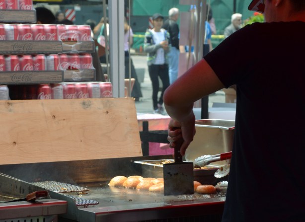 under a tent roof, a man is cooking burgers