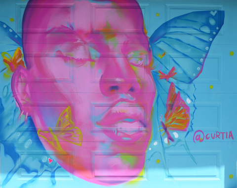 mural on a garage door with large pink face, eyes closed, butterflies flying around