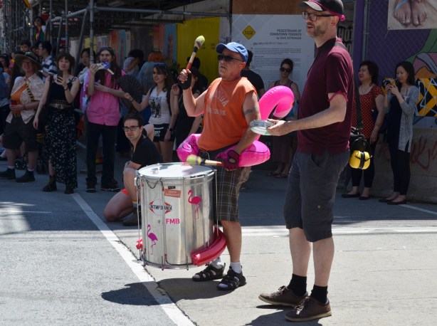 a man plays a drum on the sidewalk, on parade route