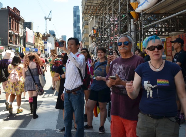 spectators on the sidewalk on Yonge street as dyke march passes by