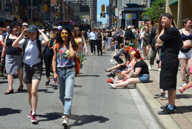 dyke march, walking down Yonge street with people sitting on the sidewalk watching the parade
