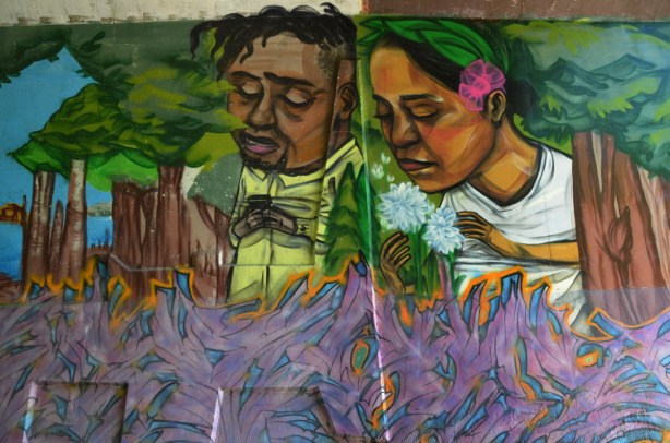 part of an elicser mural beside West Highland Creek, under Lawrence Ave., a young couple, she has a pink flower in her hair 