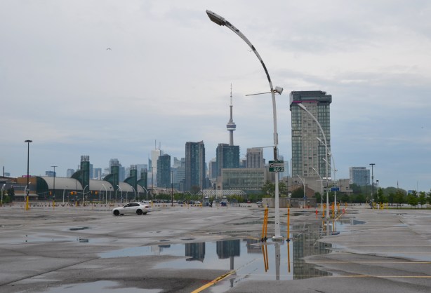 CNE parking lot, empty except for one white car, large puddles with reflections, and the city in the background, CN TOwer, tall buildings, 