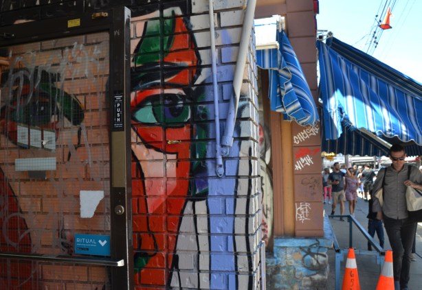 mural of a large face with eyes looking outward, looking onto the street where there are people passing by, Kensington storefront 