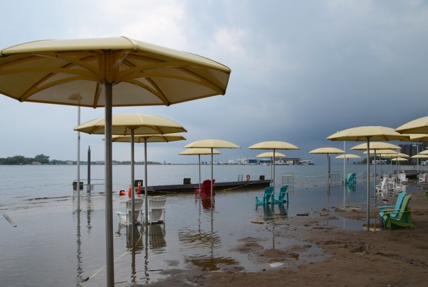Toronto waterfront showing flooding at H 2 O park with its Muskoka chairs and yellow umbrellas, dark skies in the distance as a storm approaches 