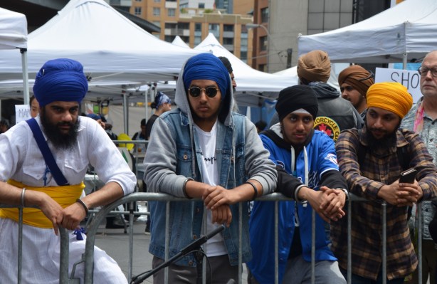 At Turbanup event at Yonge Dundas Square, 4 young men standing behind a barricade, all with turbans, one with a hoodie over his turban