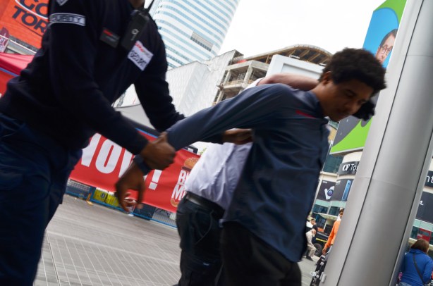 a young man is being grabbed and held on to by two security guards and they are removing him from Yonge Dundas square
