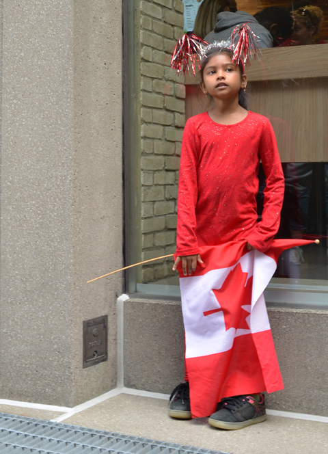 Raptors fans celebrating team's NBA championship, parade day in Toronto, a girl with red and white streamers on her head, dressed all in red, and holding a Canadian flag 