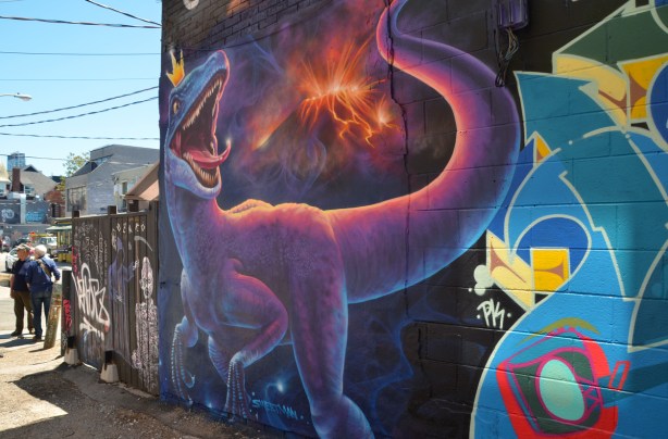on a Kensington wall, a large mural of dinosaur on a black background it's wearing a small gold crown with 3 points, 