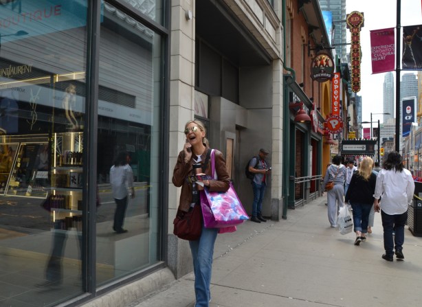 a woman is laughing as she talks on her phone and walks up Yonge Street
