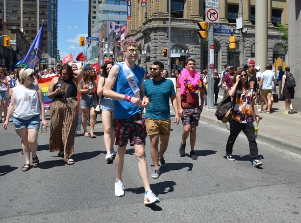 a young man in a pink crown and banner that says future bride, walks with a group of other people in a dyke march on Yonge street