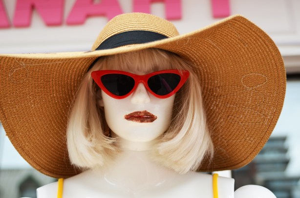 head of a mannequin with large brim hat, shoulder length blond hair, red sunglasses, lipstick 