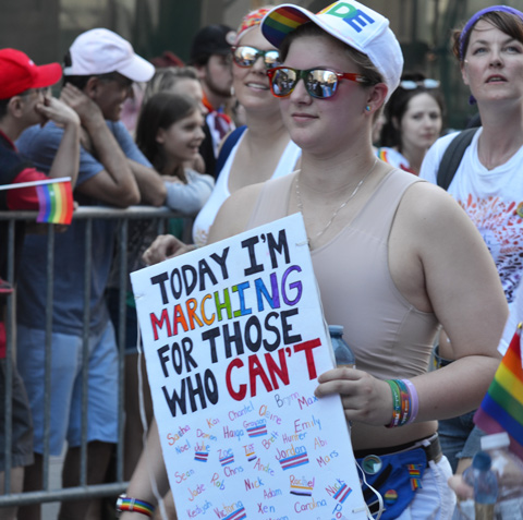 a person walking the pride parade carrying a sign that says I am marching for those who can't