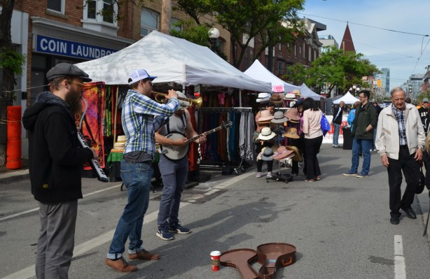 three musicians playing on the street, open violin case on the ground to collect money, people walking by 