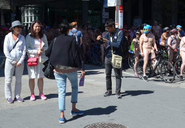 world naked bike ride and people on the sidewalk watching them