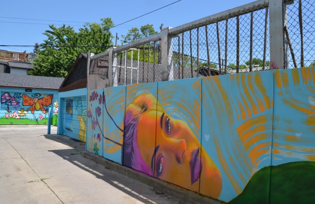 spray painted mural in a lane, woman lying on her back, orange face with pink features, 