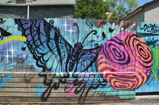 spray painted mural in a lane, butterfly and circle, on wood fence, by Oriah Scott, 