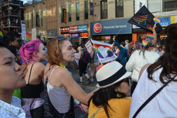 people standing on the sidewalk watching the pride parade 