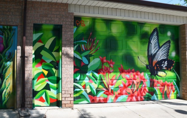 small red flowers growing in bunches, in a mural, along with a butterfly, on a garge door