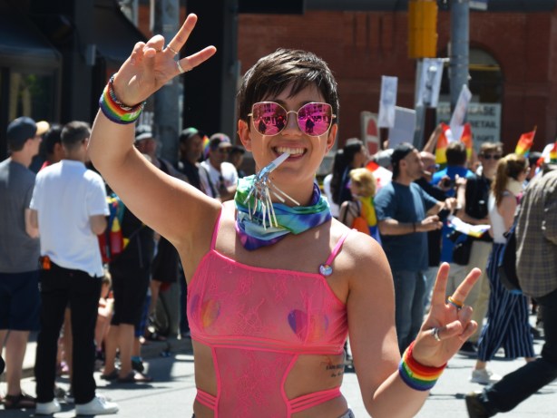dyke march, woman in pink rimmed glasses holds fingers in peace symbol