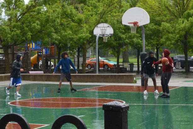 four boys playing basketball on a green and brown court, in the rain, 