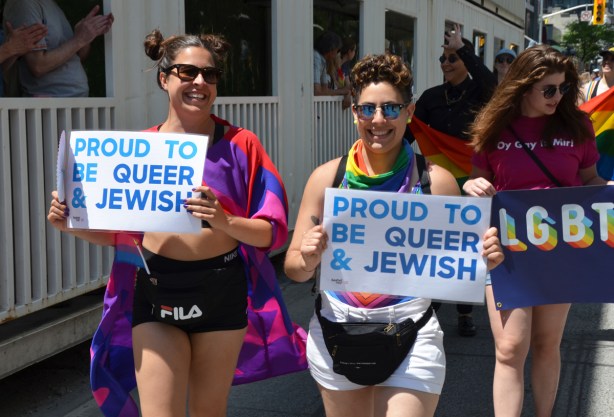two women in dyke march with signs that say proud to be queer and Jewish