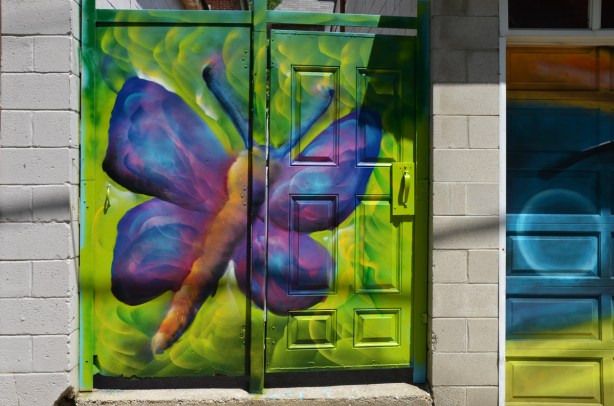 spray painted mural in a lane, purple butterfly,on bright green, covering two doors