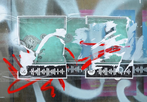 posters on a window that have been partially ripped and streaks of red paint sprayed on them, also white spray paint 